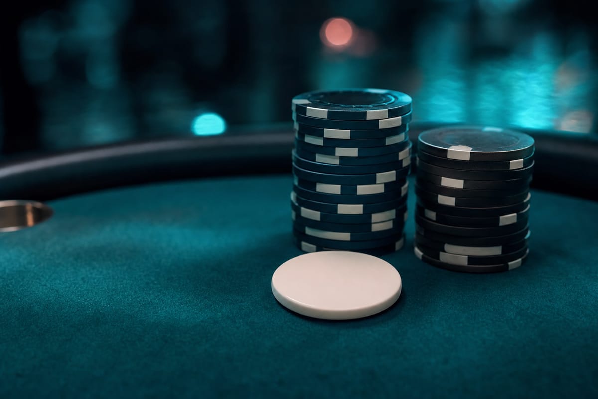 Plain white dealer button in front of two stacks of dark chips with white edge spots on teal felt (AI-generated image)