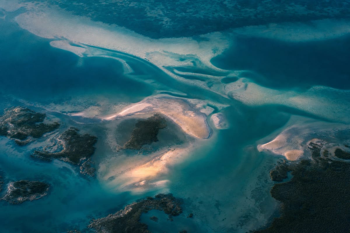 Aerial view of a lagoon with pale sandbanks, winding turquoise channels and dark patches of reef (AI-generated image)